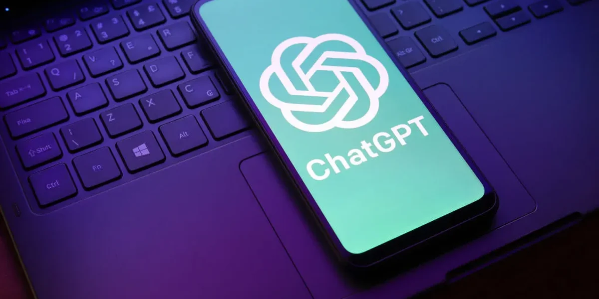 Un telefon pe tastatura unui laptop, cu logo-ul și numele ChatGPT pe ecran