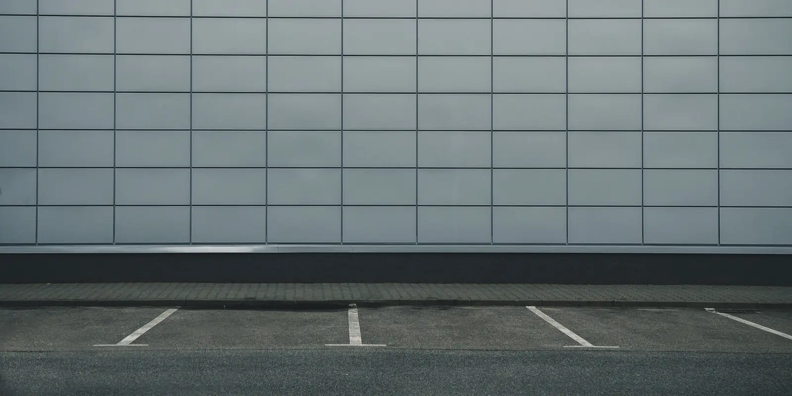 Empty car park in front of a grey panelled wall, three bays marked out in white paint and not a single car