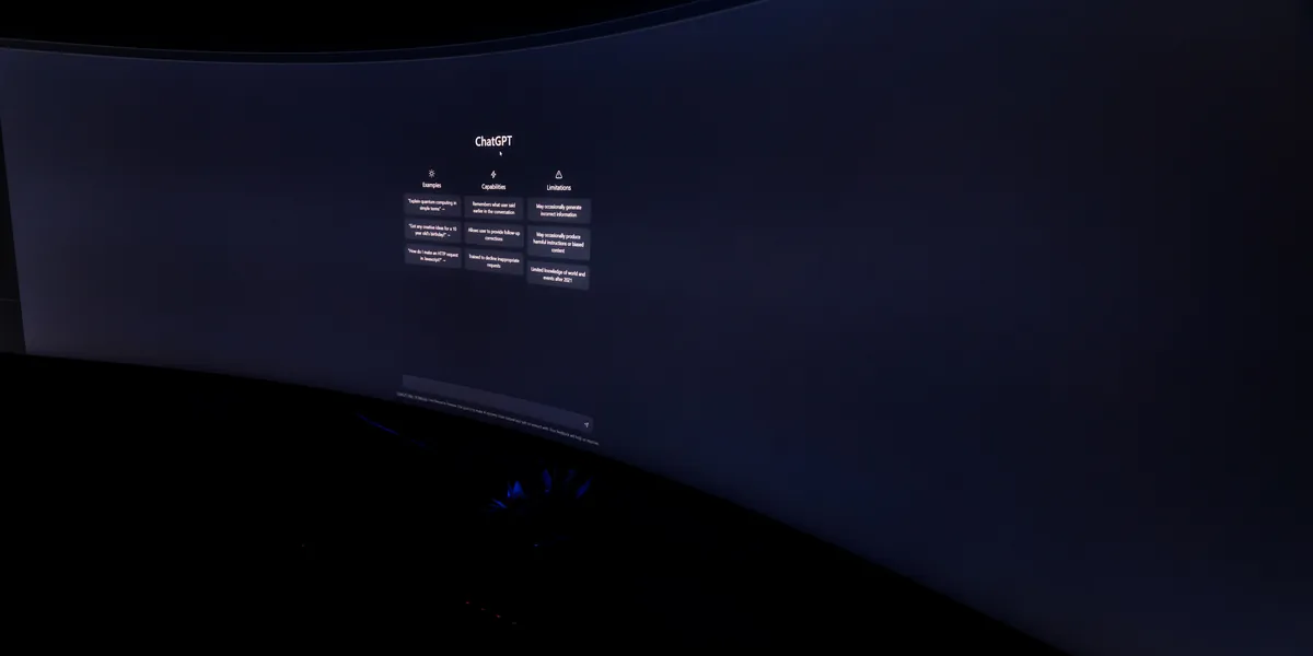A curved computer monitor in a dark room showing the ChatGPT start screen, the interface text too small to read