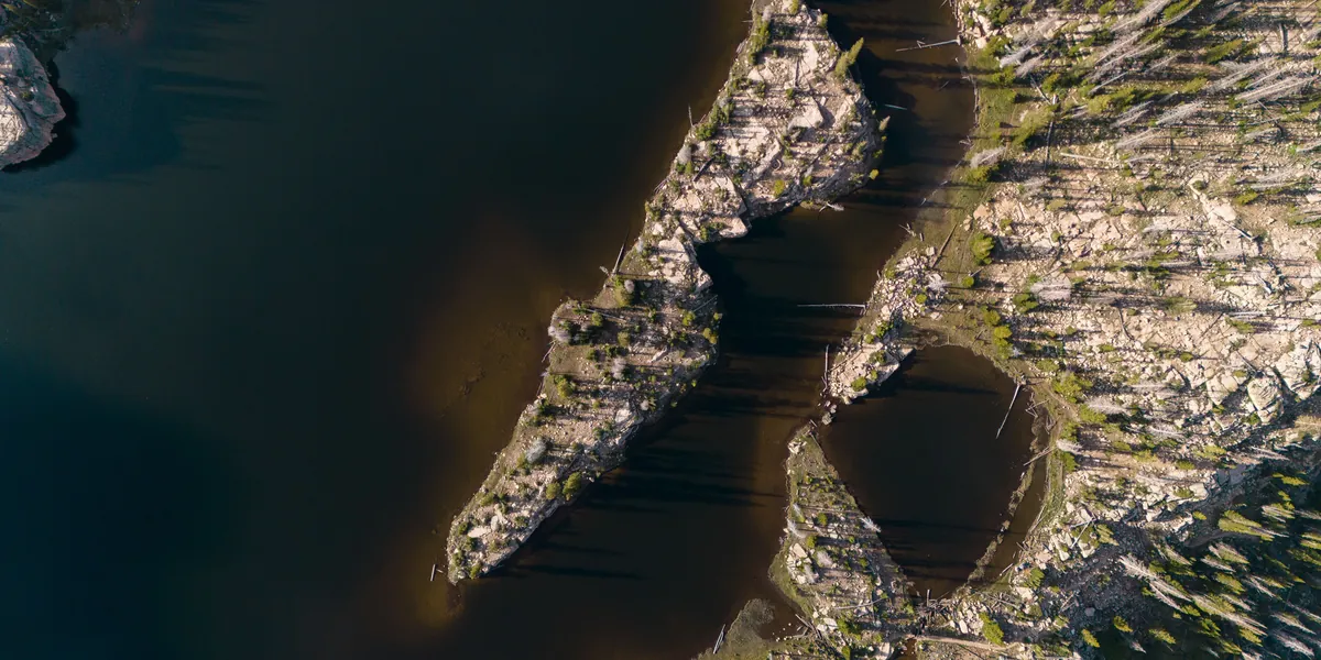 Aerial view of a rocky shoreline meeting dark water, the boundary between land and lake clearly visible from above