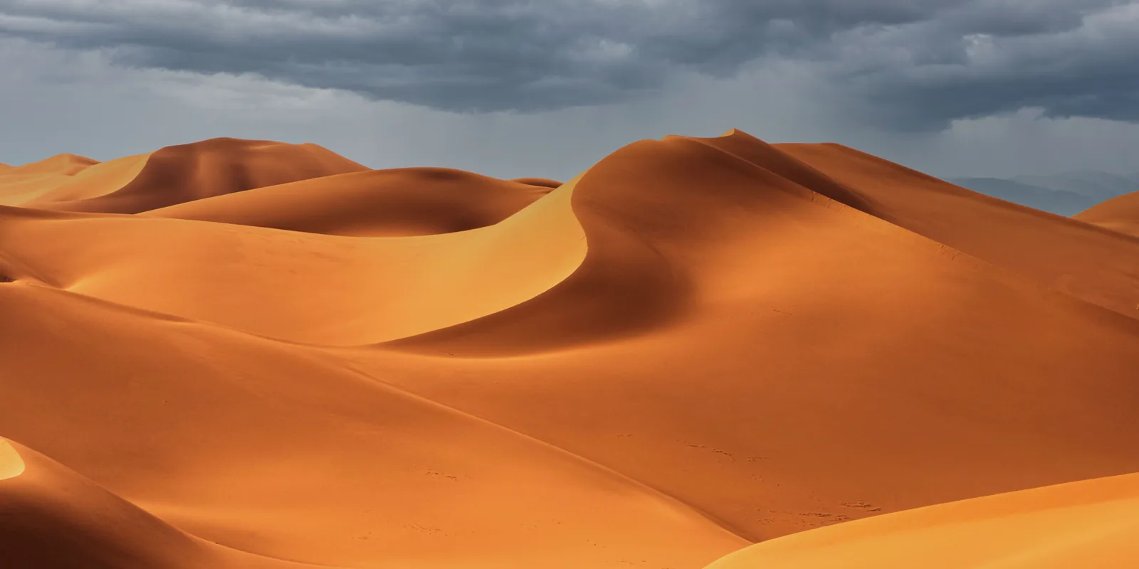Sand dunes under a heavy grey sky, photographed from a distance, with no landmarks or signposts