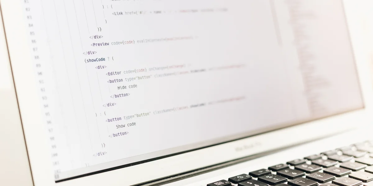 Schermo di un portatile con codice sorgente di una pagina web: tag HTML e frammenti JavaScript a fuoco, tastiera in primo piano