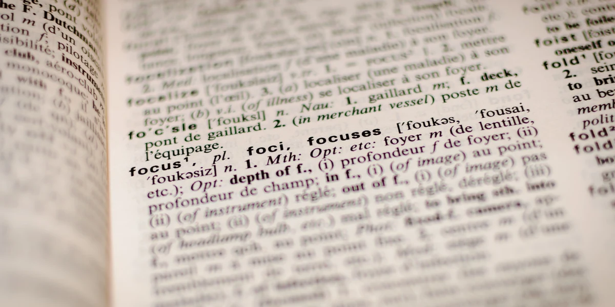 Close-up of a bilingual dictionary page with the entries focus, foci, focuses and fo'c'sle in focus and the rest of the column blurred
