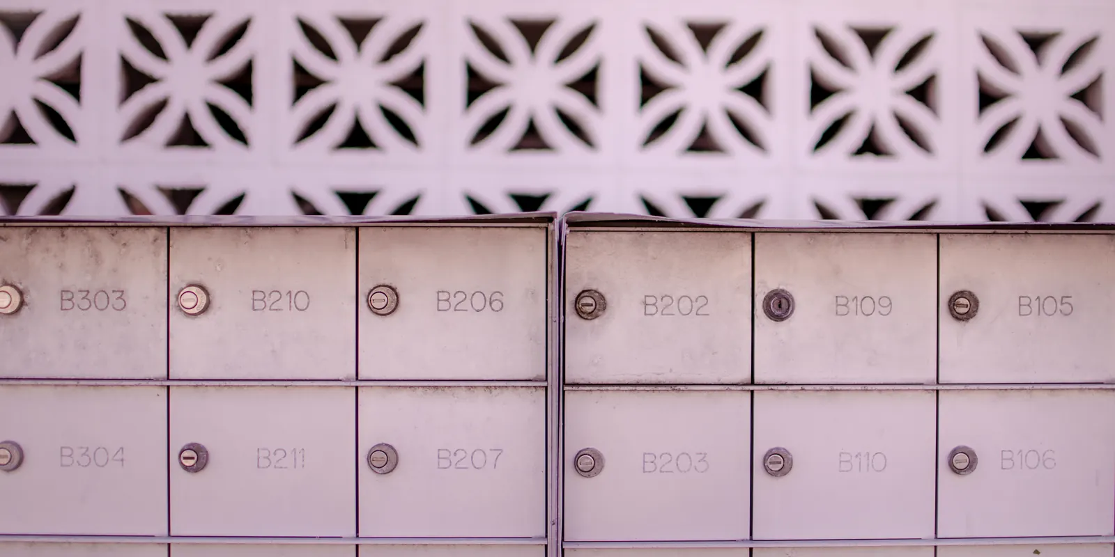 Wall of pale pink post office boxes stamped B303, B210, B206, B202, B109, B105 on the top row and B304, B211, B207, B203, B110, B106 below