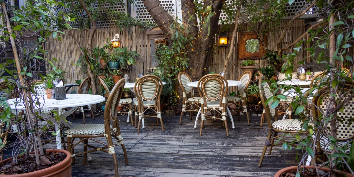 O terasă goală cu mese albe, scaune de bistrou și plante în ghivece, fotografiată fără oameni