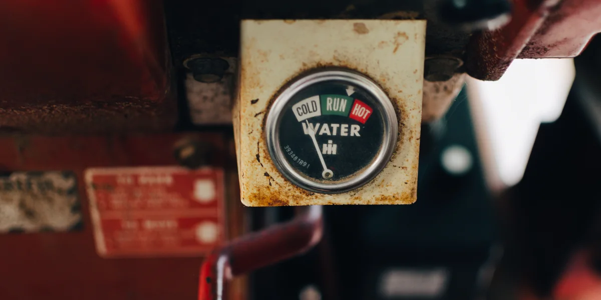 Ceas de bord ruginit pe un utilaj agricol, cadran cu benzile COLD, RUN și HOT sub cuvântul WATER, acul oprit la rece