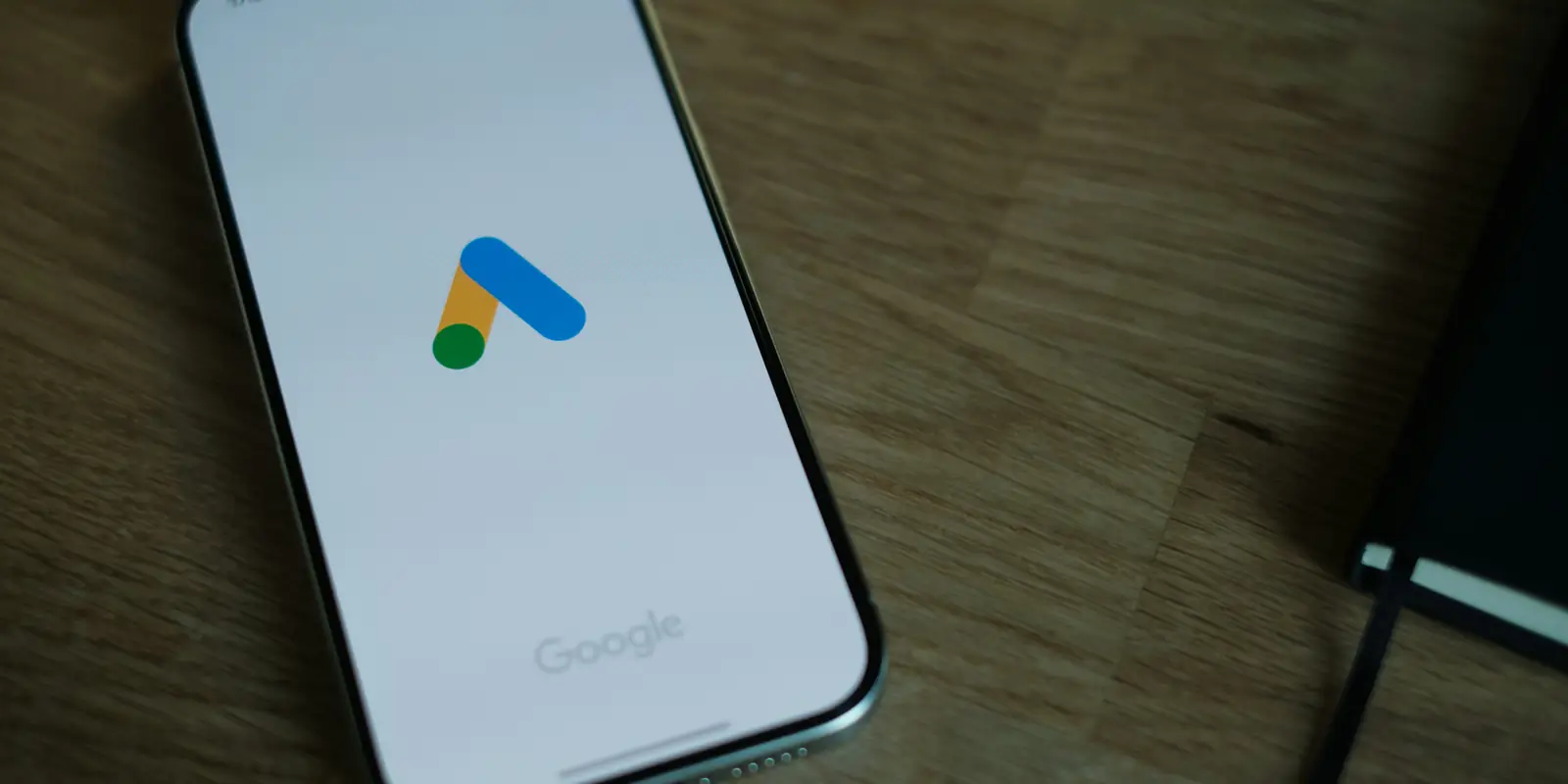 Telefon pe un birou de lemn, cu sigla Google Ads pe ecran