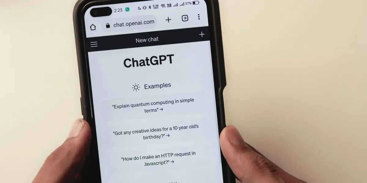 Two hands holding a black phone with ChatGPT open in a browser at the new chat screen, three example prompts listed below and the battery indicator at 37 per cent