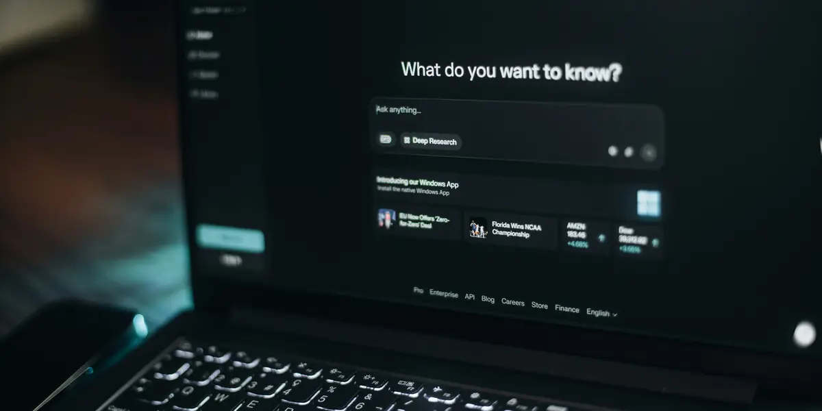 A laptop screen in a dark room showing the Perplexity interface open on the prompt What do you want to know, with a text input box and a Deep Research button