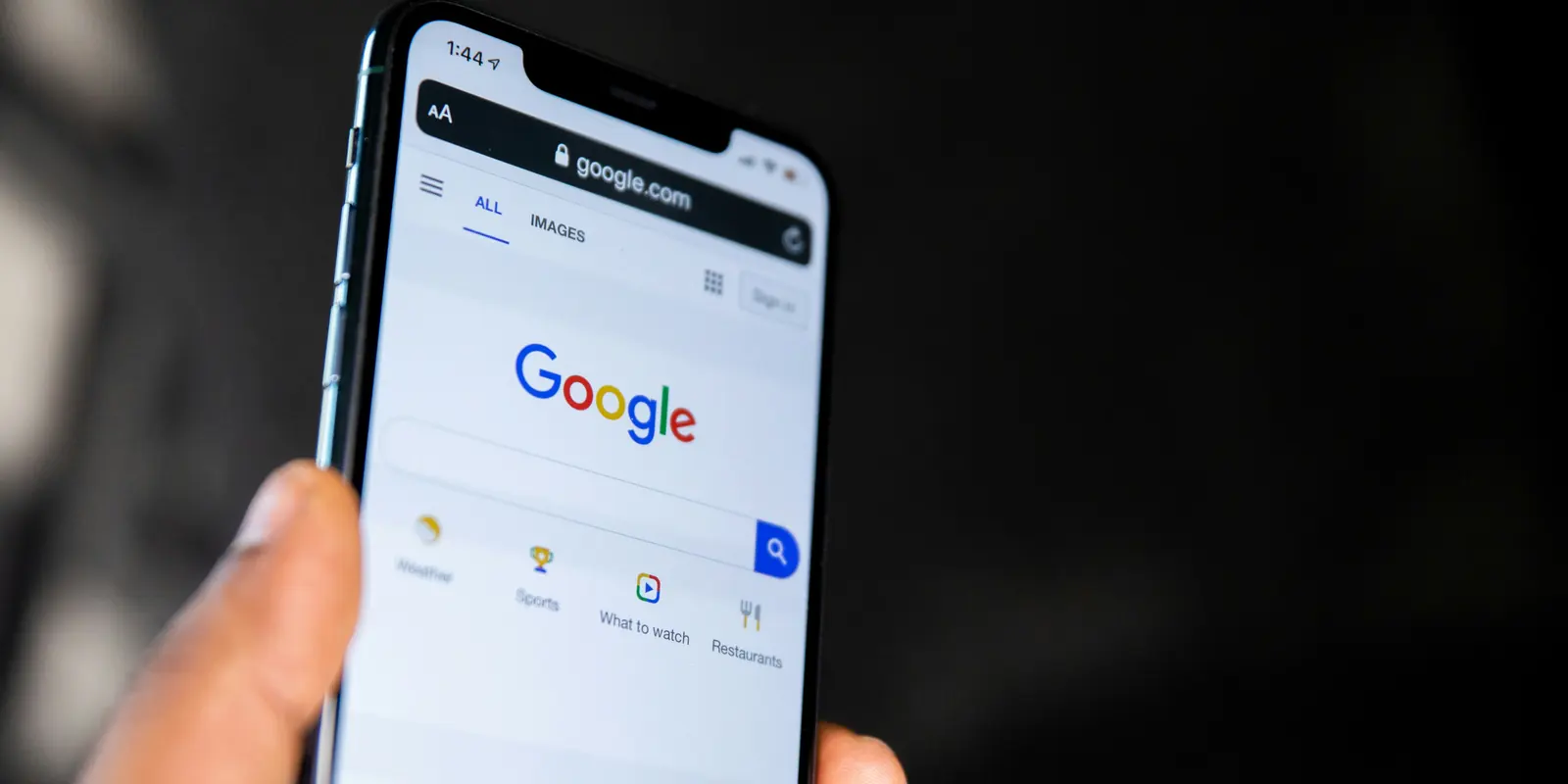 A hand holding a phone with the Google search page open