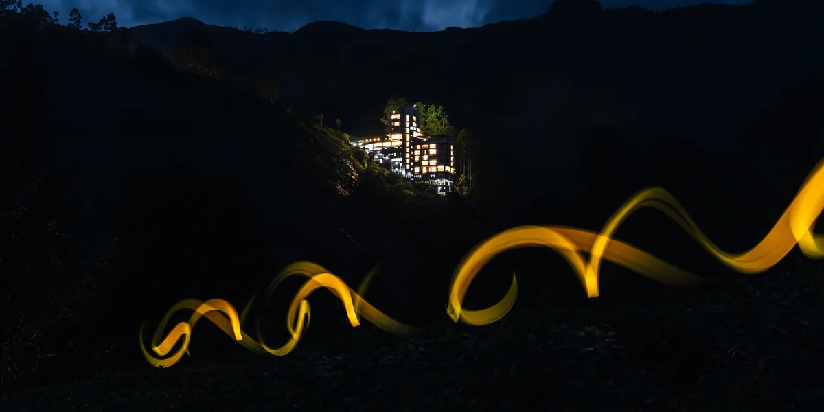 A golden trail of light in the dark, in front of a black hillside with one lit building