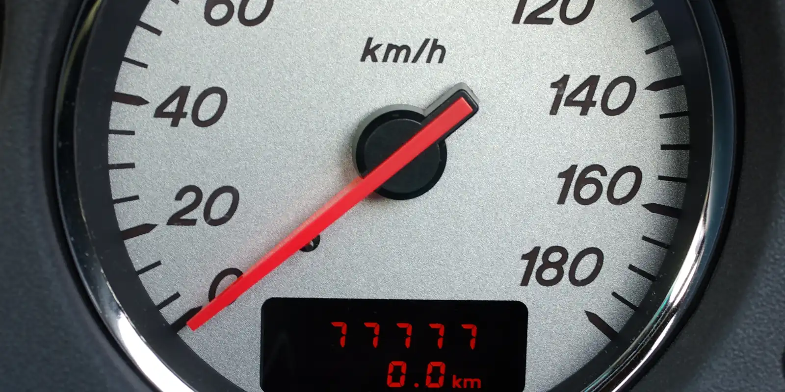Vitezometru analogic în prim-plan, cu scala de la 20 la 180 km/h, acul roșu oprit la zero și afișaj digital pe care se citesc 77777 și 0,0 km