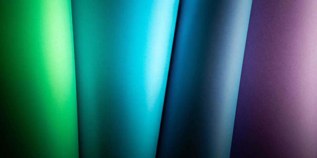 Rolls of coloured paper standing side by side, photographed close up, forming a continuous scale of tones from green through blue to violet