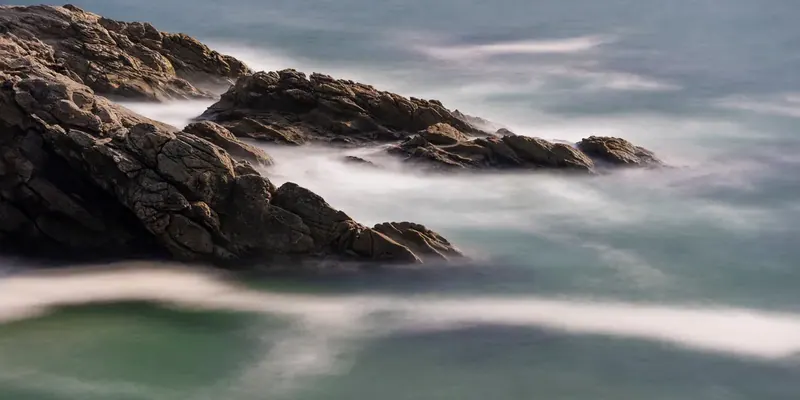 Rocks on a sea shore in a long exposure, the waves turned into white mist flowing between them