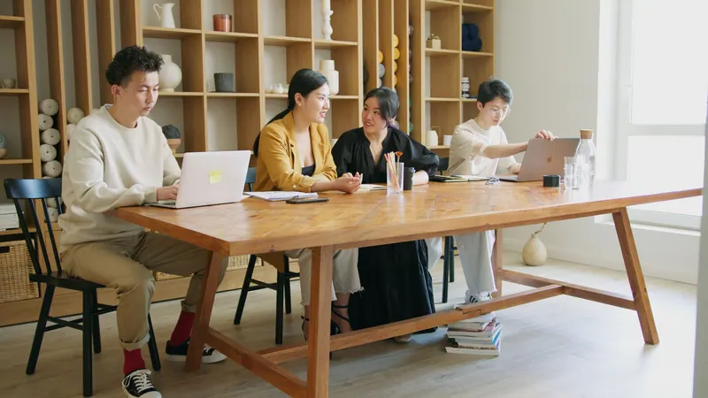 A team at a long wooden table, working together on laptops